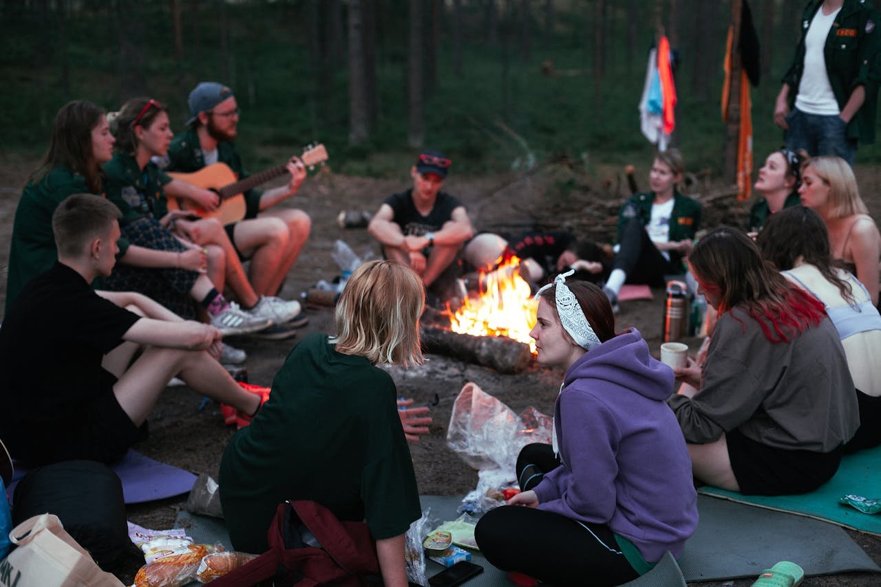 Een diverse groep genietend van samenhorigheid, gitaar en een kampvuur in de avond.